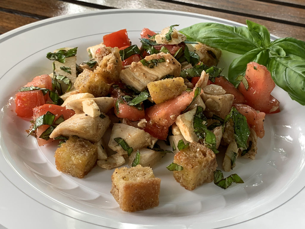 Chicken Panzanella (chicken, tomatoes, basil, onions and croutons) on a white plate.