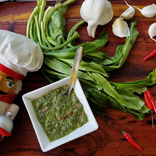 Culantro leaves, garlic cloves, whole red Thai chilies and a small white dish with a green sauce, all sitting on a pretty wood board. There's a nutcracker in the foreground who looks like a chef.
