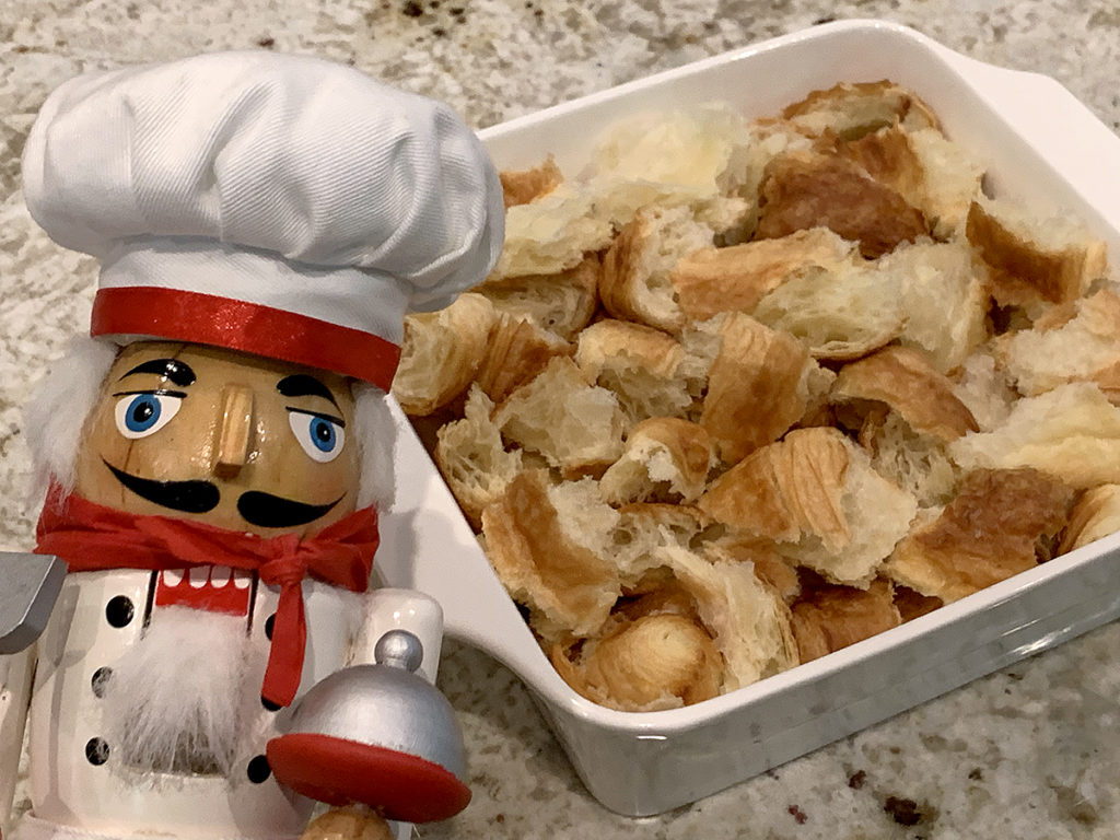 Large chunks of croissants in a square, white dish with a nutcracker who looks like a chef in the foreground.