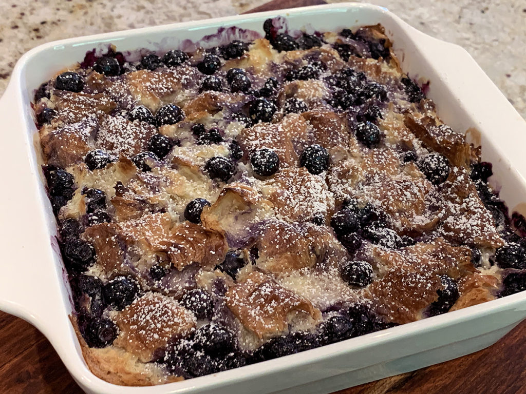 Baked blueberry & cream cheese croissant puff dusted with powder sugar in a white square casserole dish.
