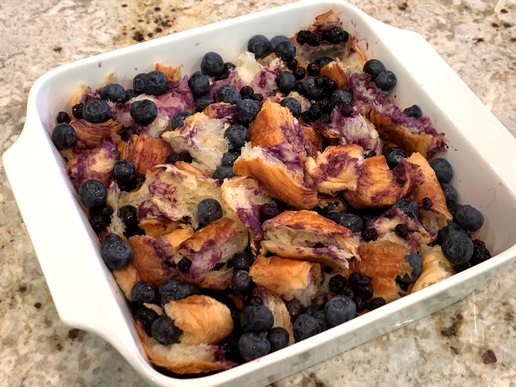 Blueberries and croissant pieces in a white square casserole dish.