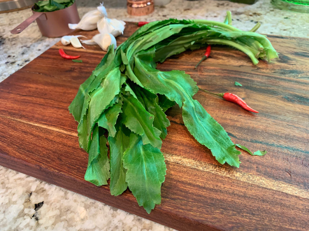 Culantro leaves, garlic cloves, whole red Thai chilies all sitting on a pretty wood board. 