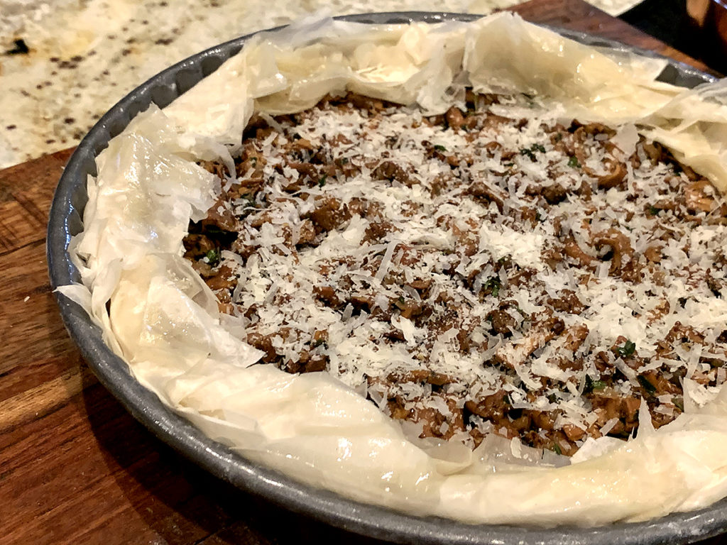 Chanterelle duxelles in a round tart pan with ruffled filo dough around the edges and cheese sprinkled on the top, ready for the oven. 