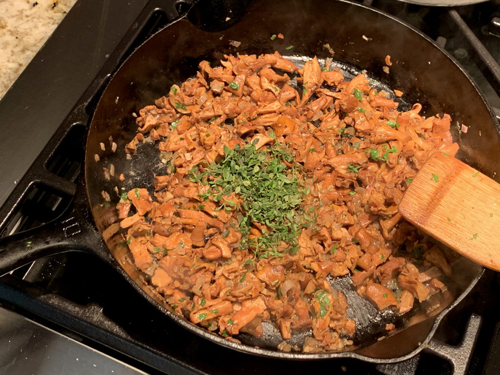 Sauteed chanterelles with a bit of fresh chopped thyme on top, in an iron skillet with a wooden spatula.