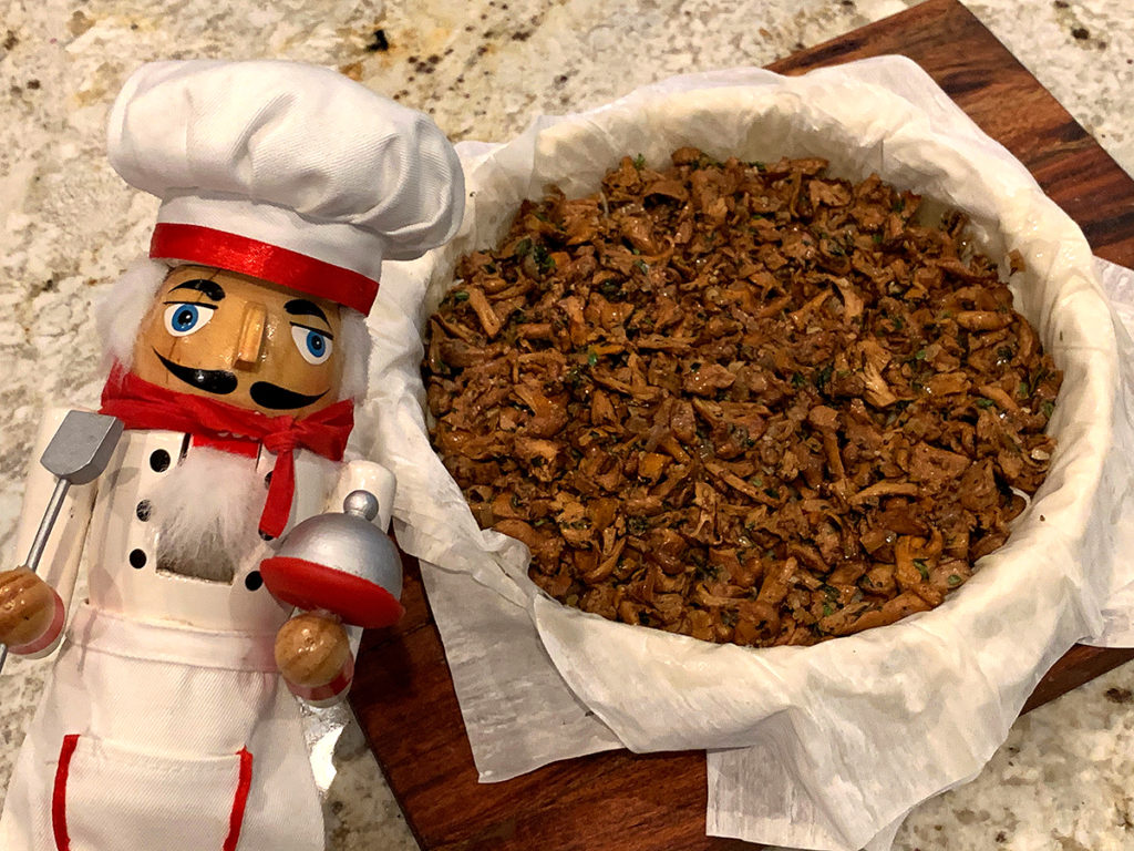 Chanterelle duxelles on multiple layers of phyllo dough in a tart pan. There's a nutcracker who looks like a chef in the foreground. 