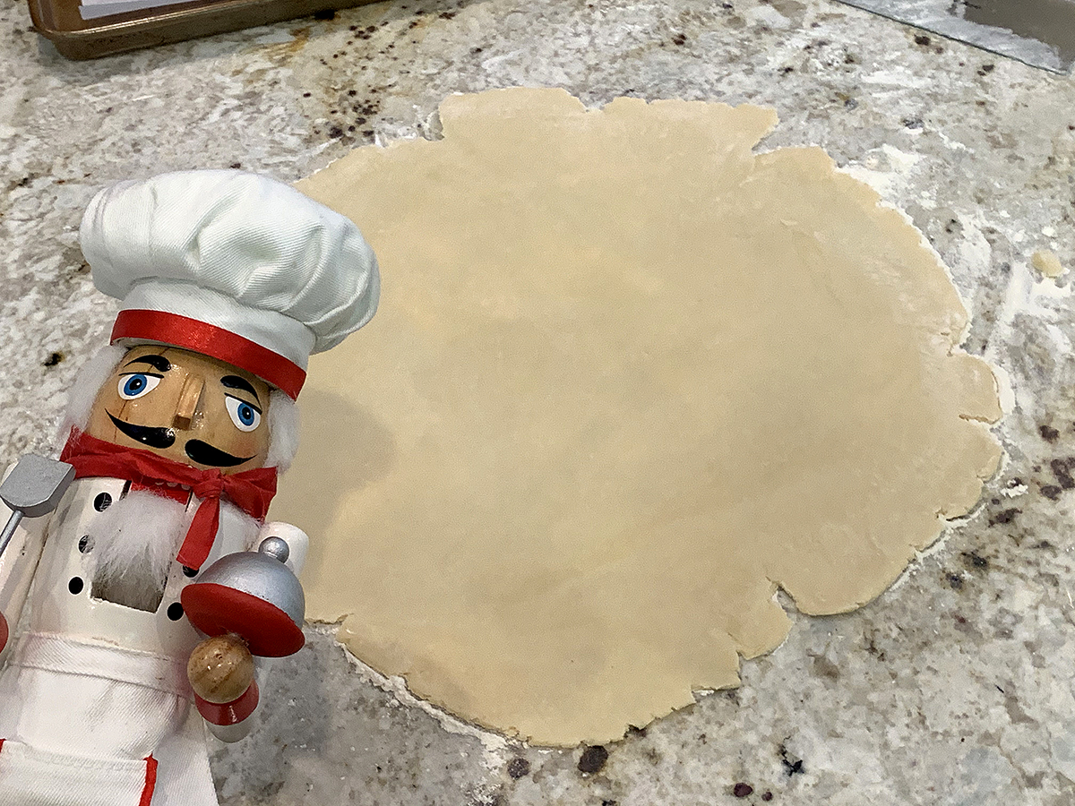A large round piece of dough that has been rolled out. There's a nutcracker who looks like a chef in the foreground to the left. 