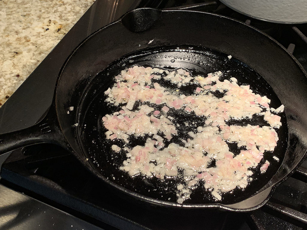 Minced shallots and garlic sautéing in an iron skillet.