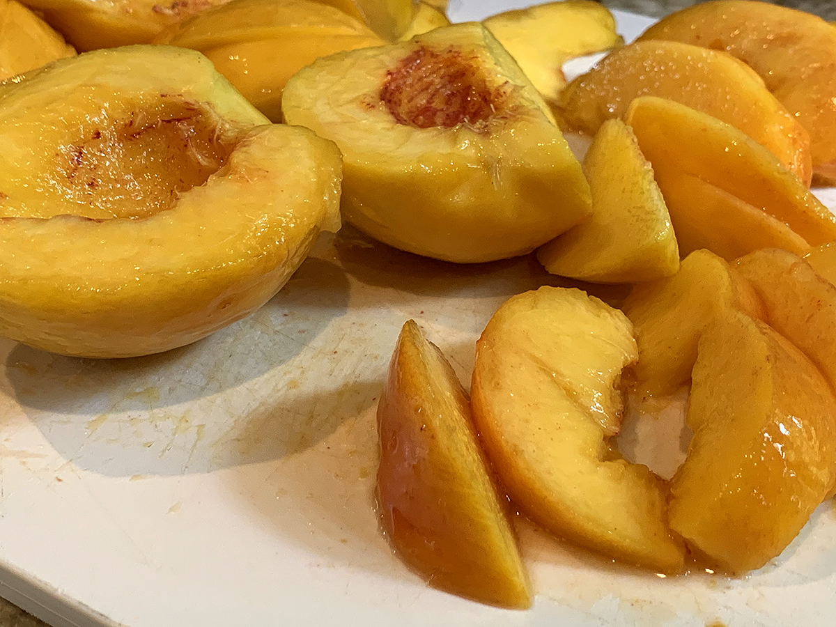 Partially sliced, peeled peaches on a white cutting board. 