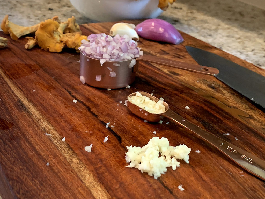 Minced shallots and garlic on a wood board.