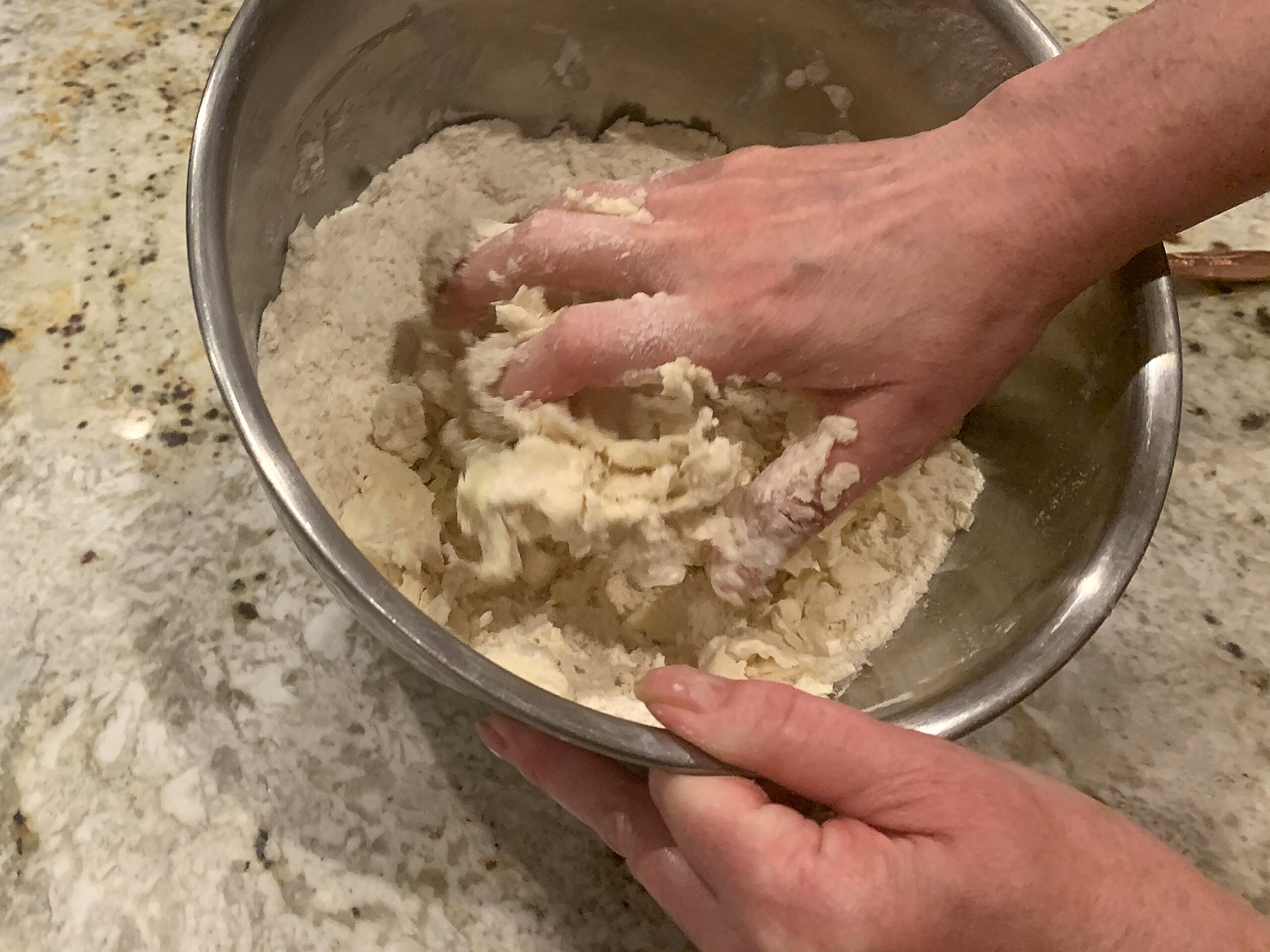 Caucasian hands mixing pastry dough in a steel bowl.