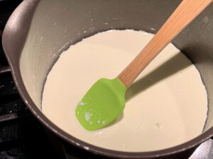 Cream in a small sauce pan with a small green rubber spatula.