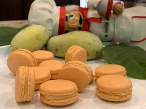 Pale orange macaron cookies on a white plate with fresh green pawpaw and a nutcracker who looks like a chef in the background.