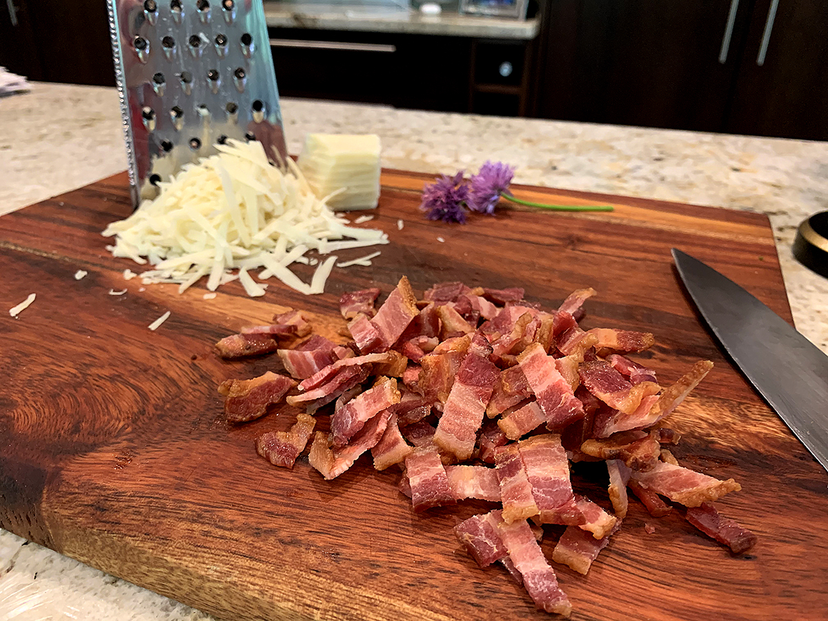 Chopped bacon and shredded cheese on a wood cutting board.