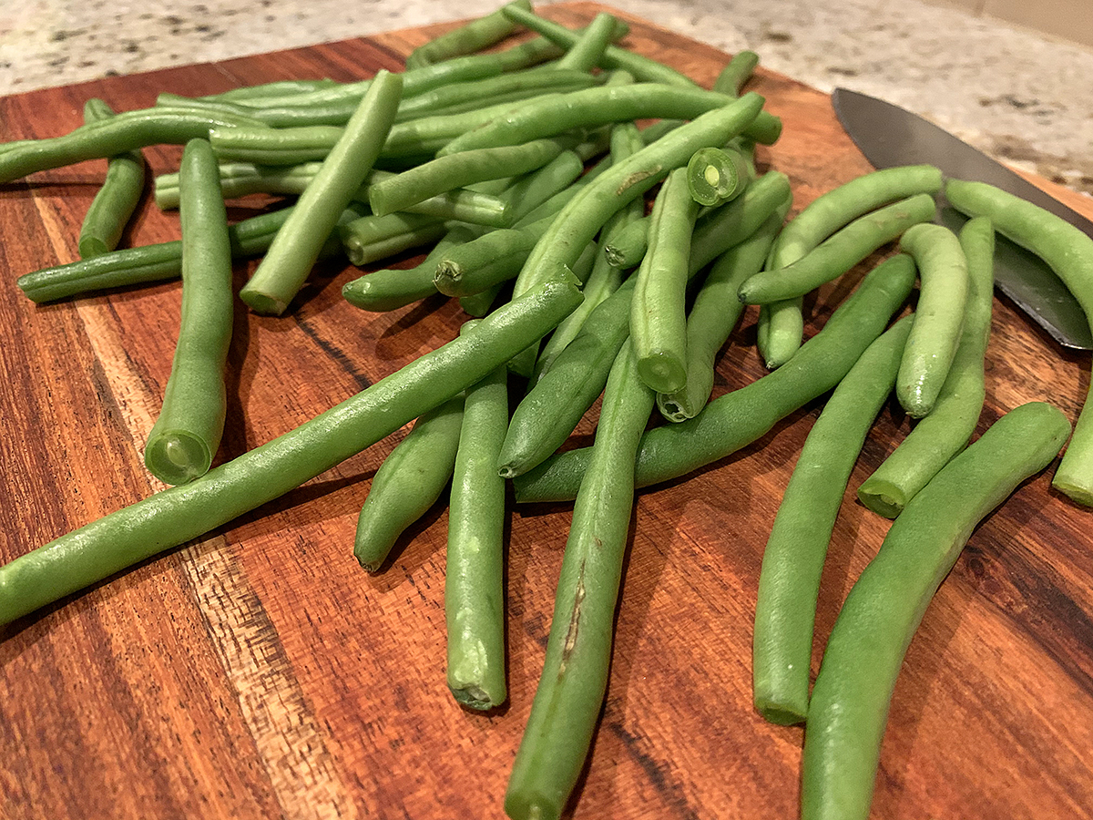 Fresh green beans on a wood cutting board.