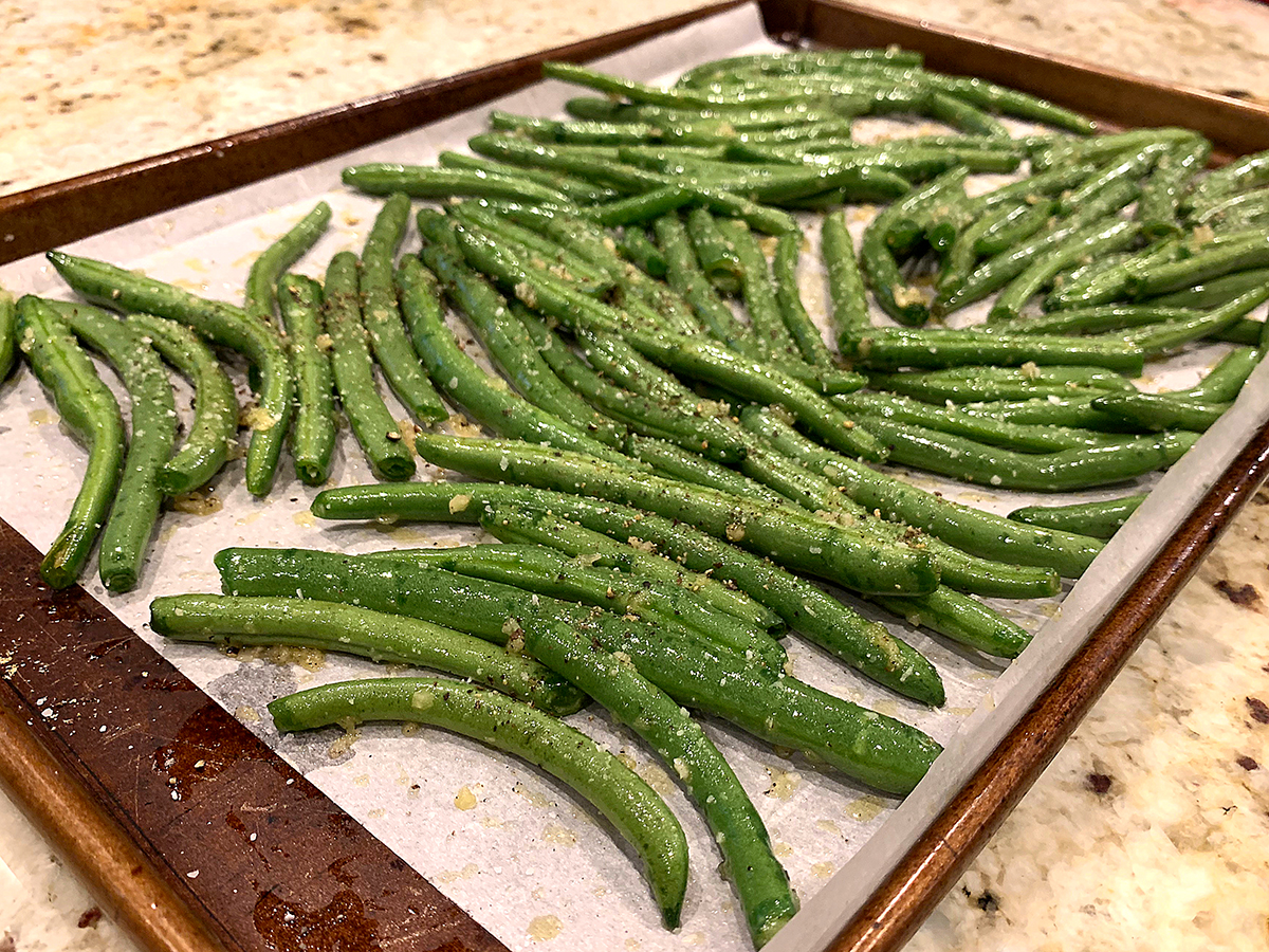 Single layer of fresh green beans on a sheet pan lined with parchment paper.