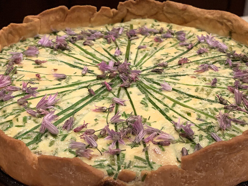Beautiful quiche garnished with fresh chives and chive blossom petals.