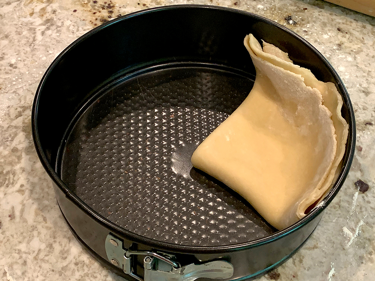Pastry dough folded in quarters and laying in a spring form pan. The corner is is the center and the edge runs up the side of the pan. It's ready to unfold.