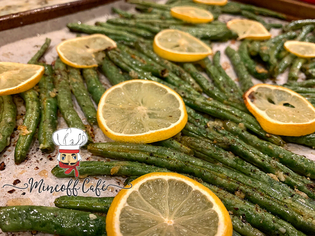 Single layer of roasted green beans with sliced lemons on top.