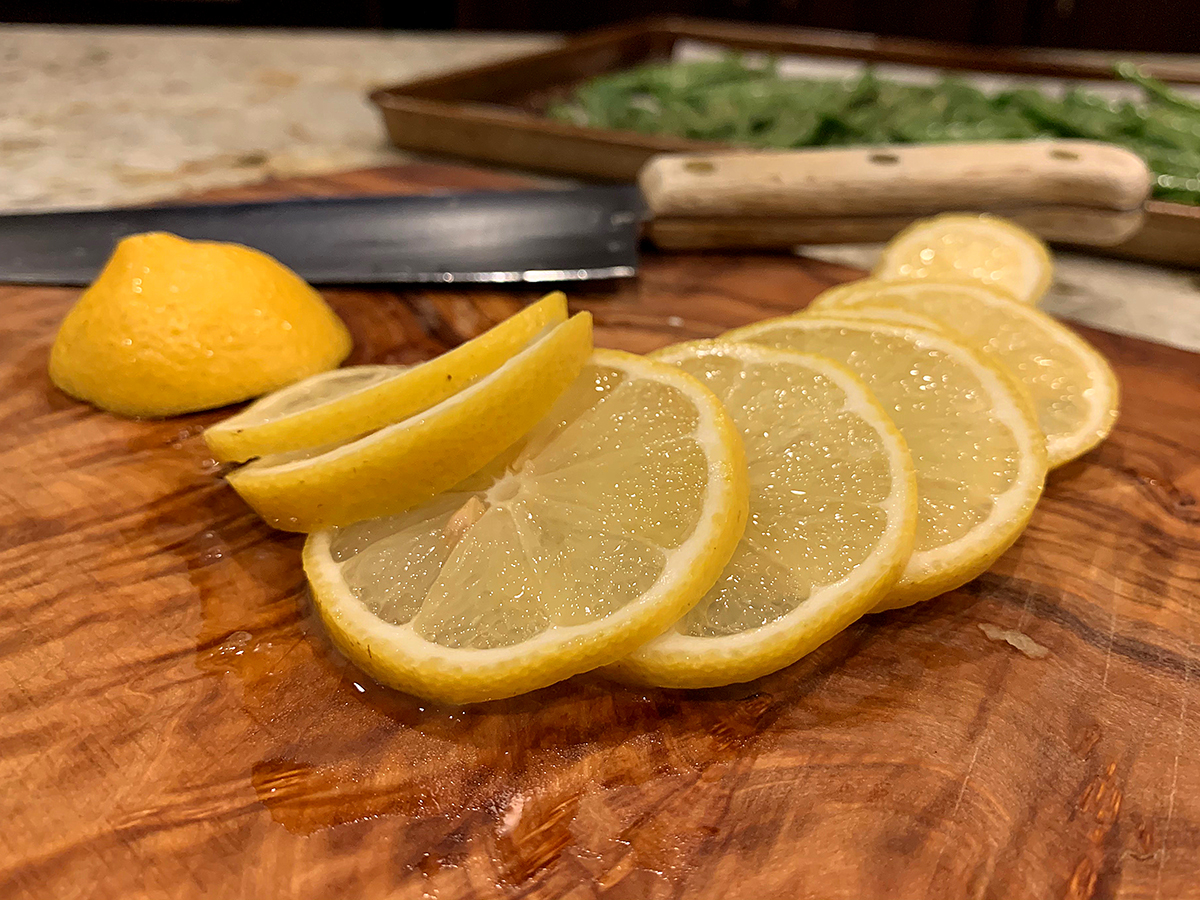 Several lemon slices on a wood cutting board.