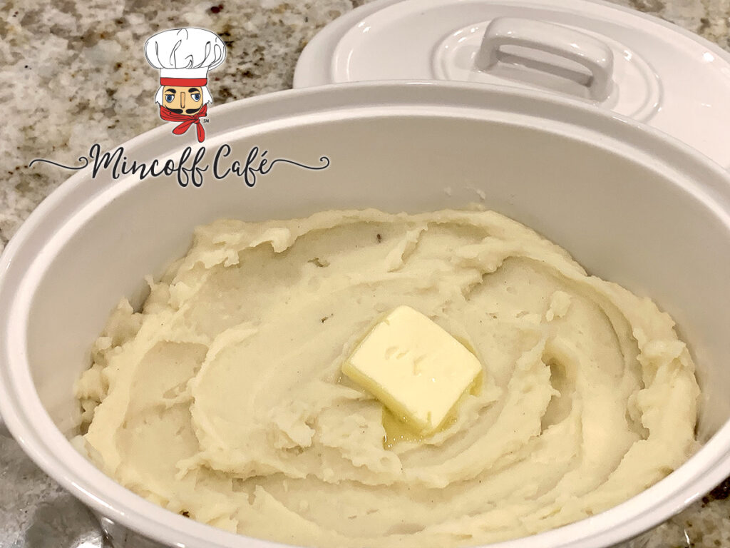 Mashed potatoes with a pat of butter melting on top, in a white bowl.