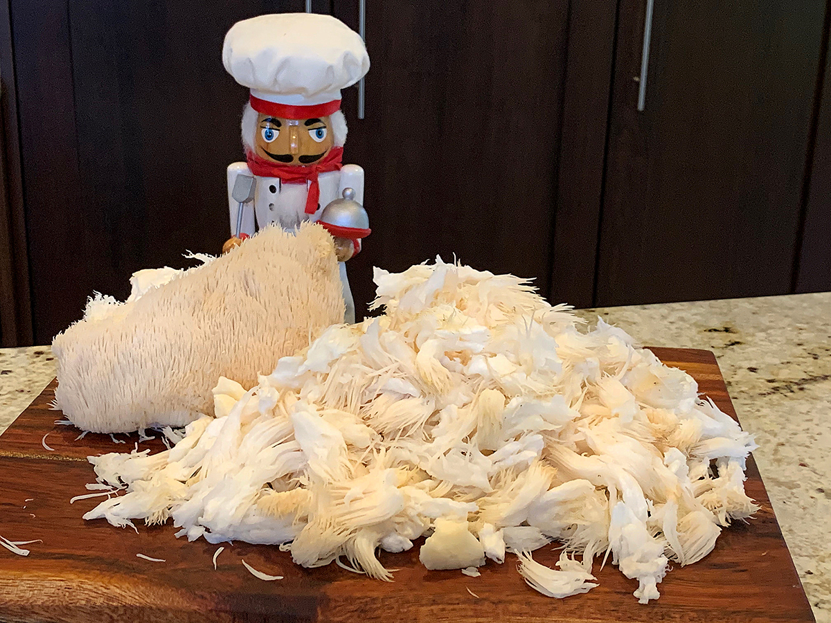 A large mound of lion's mane mushroom pieces on a wood board with another large chunk behind the pile. There also a nutcracker who looks like a chef in the background.
