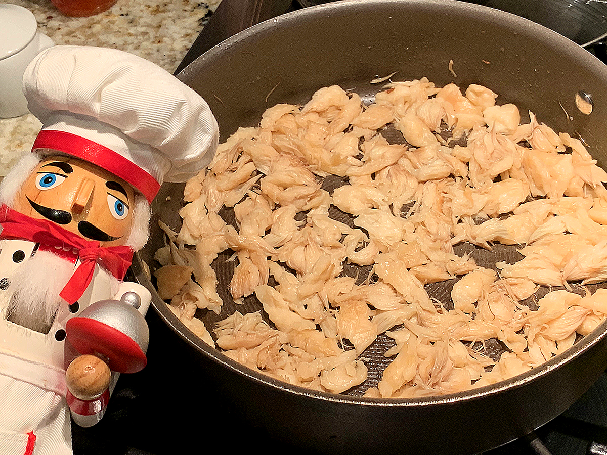 Skillet filled with slightly browned lion's mane mushroom pieces in a single layer. There's a nutcracker in the foreground who looks like a chef.