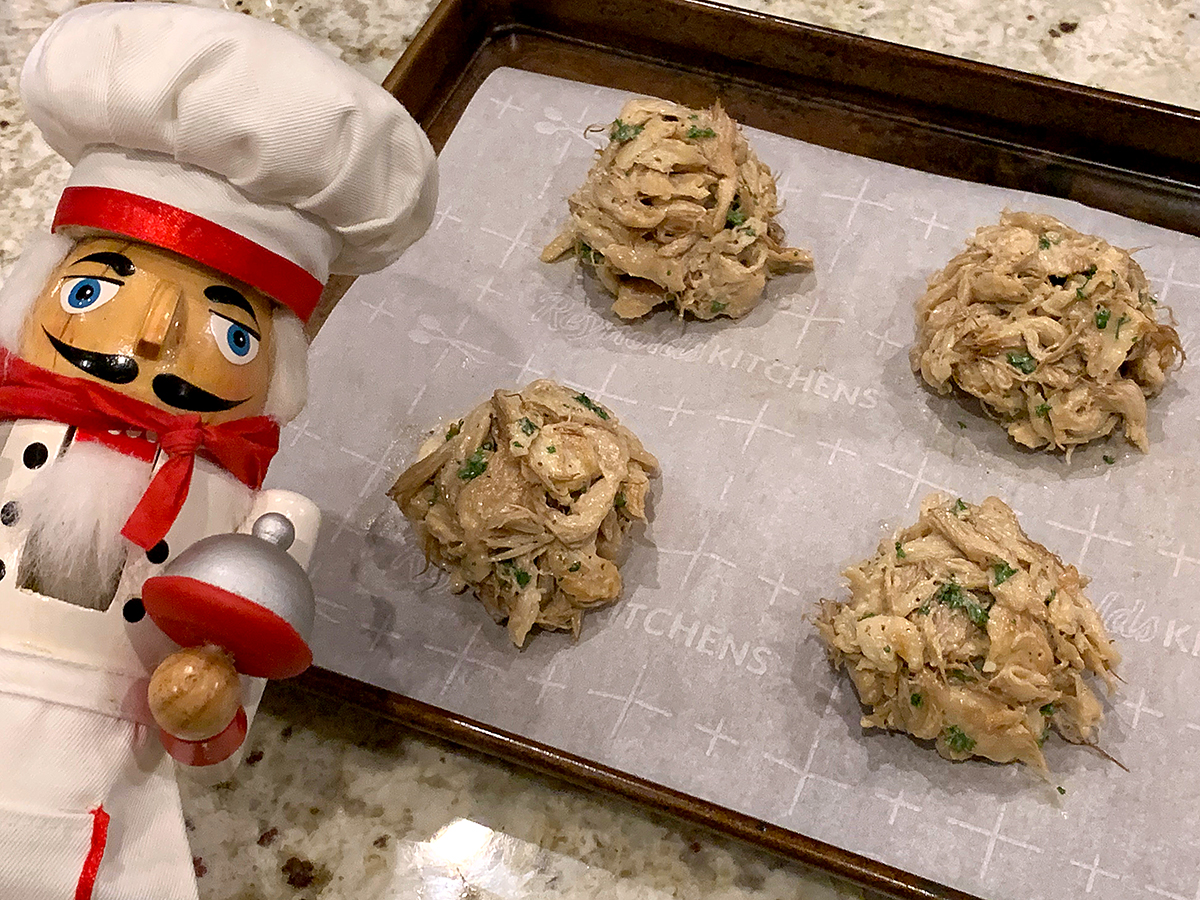 Four mounds of lion's mane "mock" crab cakes on a parchment lined sheet pan. There's a nutcracker in the foreground who looks like a chef.