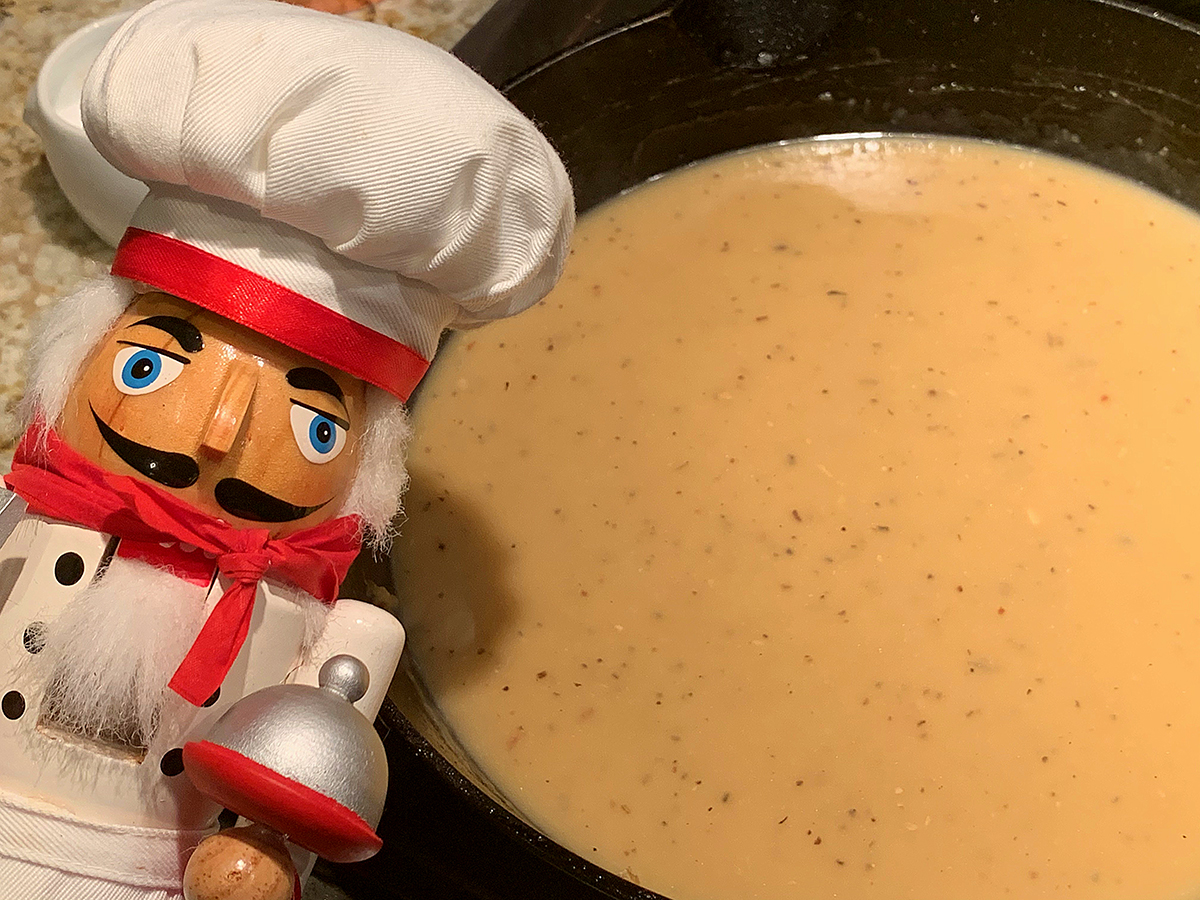 Tanish gold gravy in an iron skillet. There's a nutcracker who looks like a chef in the foreground.