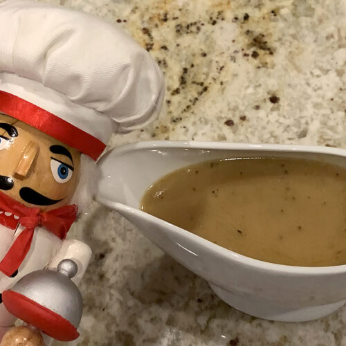 Tan gravy in a white gravy boat. There's a nutcracker who looks like a chef in the foreground.