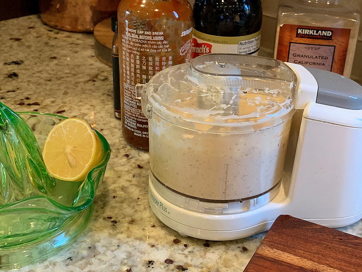 Pale orange sauce in a mini chopper, next to a green glass juicer dish with half a lemon sitting inside.