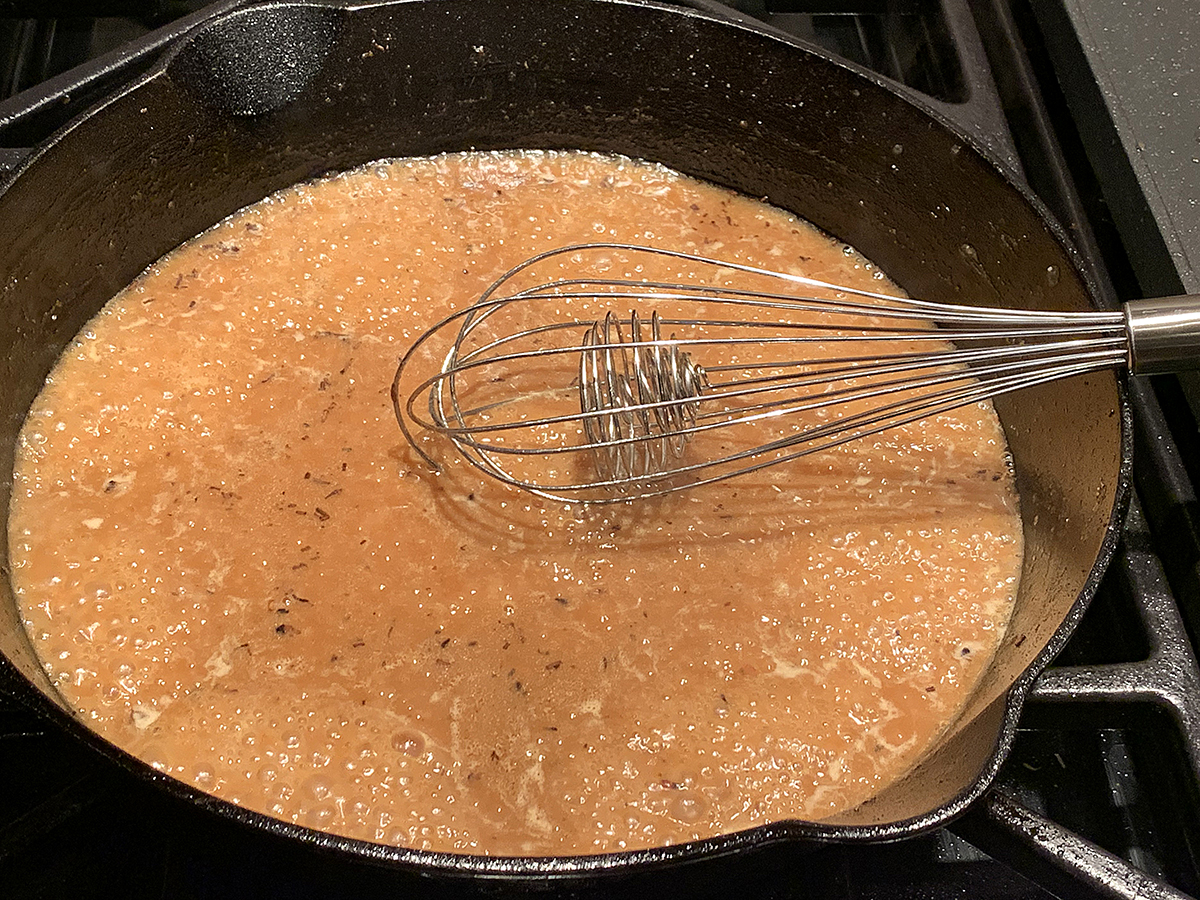 Tan bubbling gravy being whisked in an iron skillet.