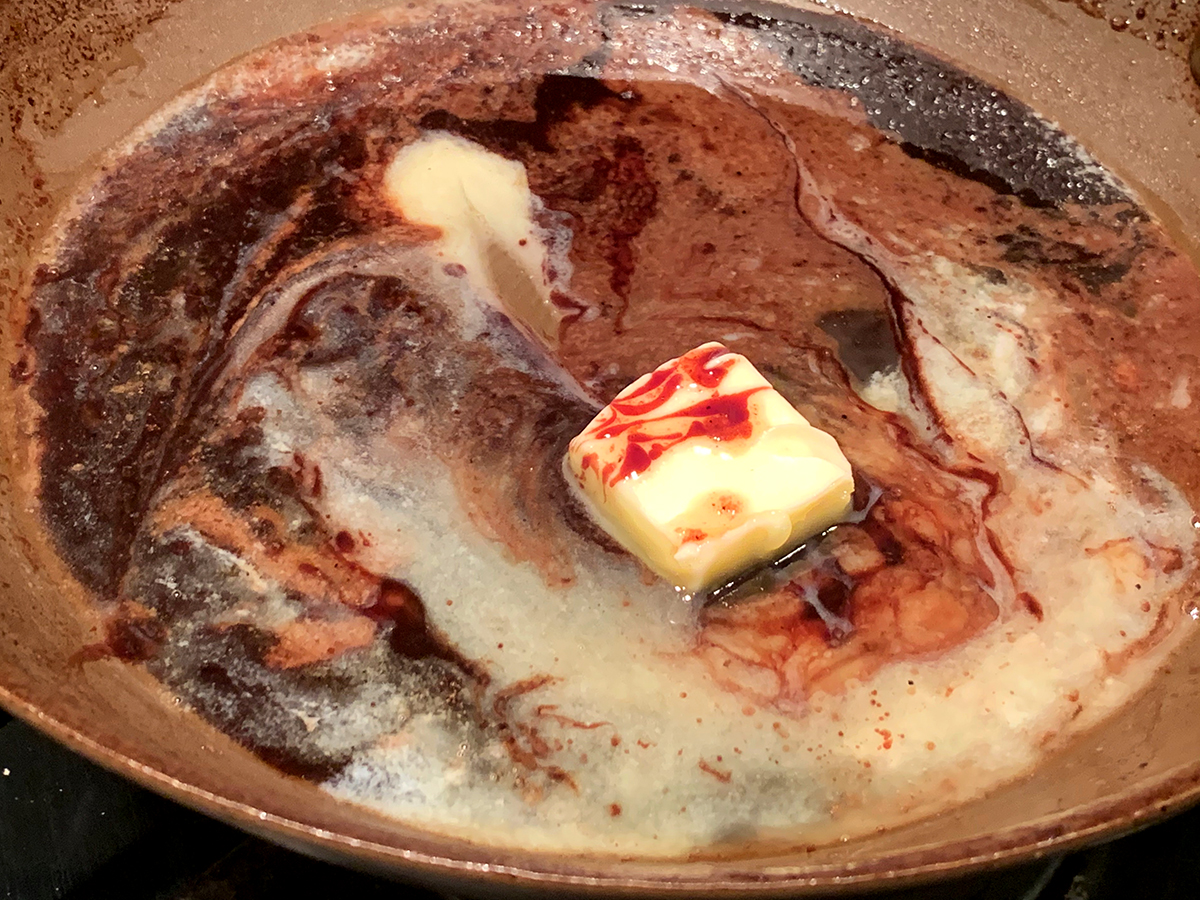 Square piece of butter melting in a pan with pomegranate wine sauce.