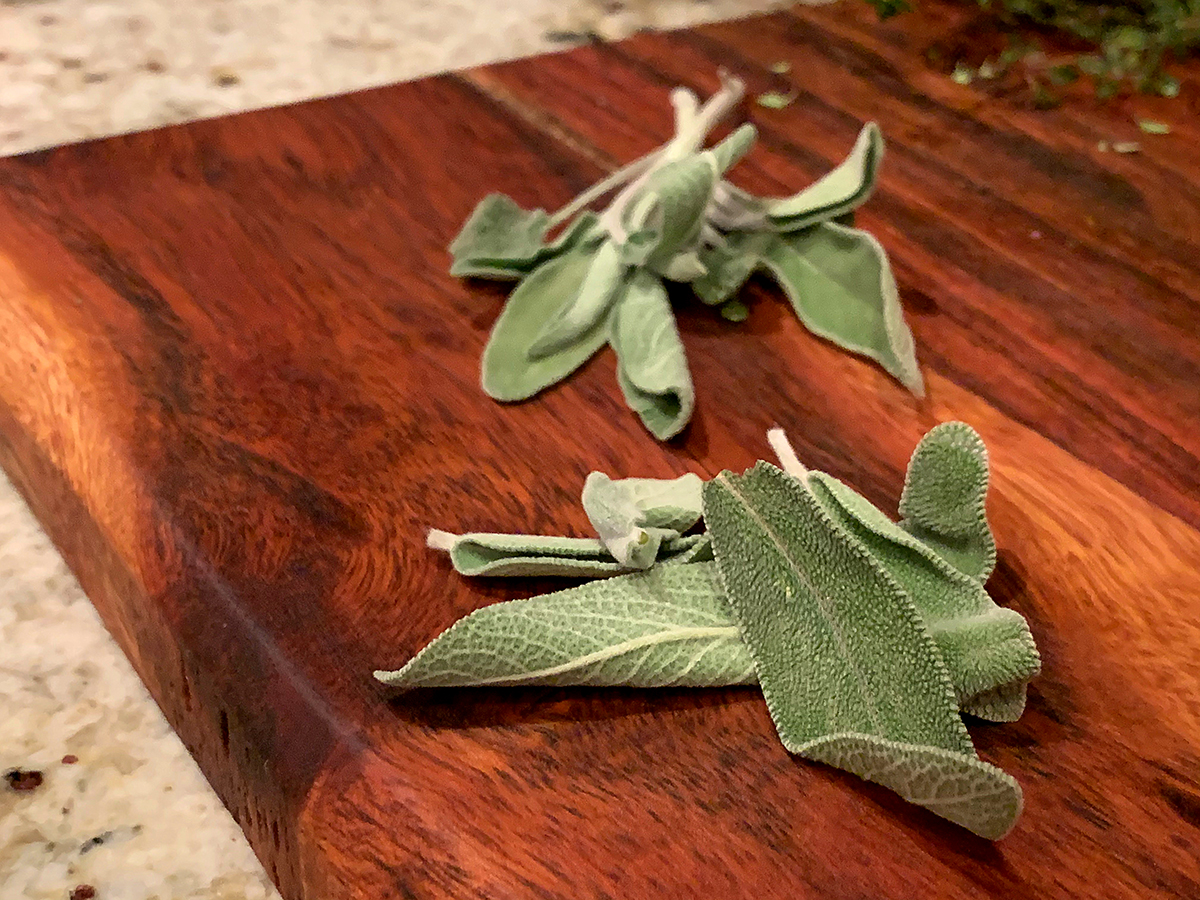 Fresh sage leaves on a wood cutting board.