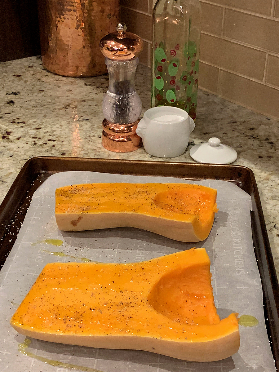 Two halves of a butternut squash, face up on a parchment lined sheet pan, seasoned with olive oil, salt and pepper.
