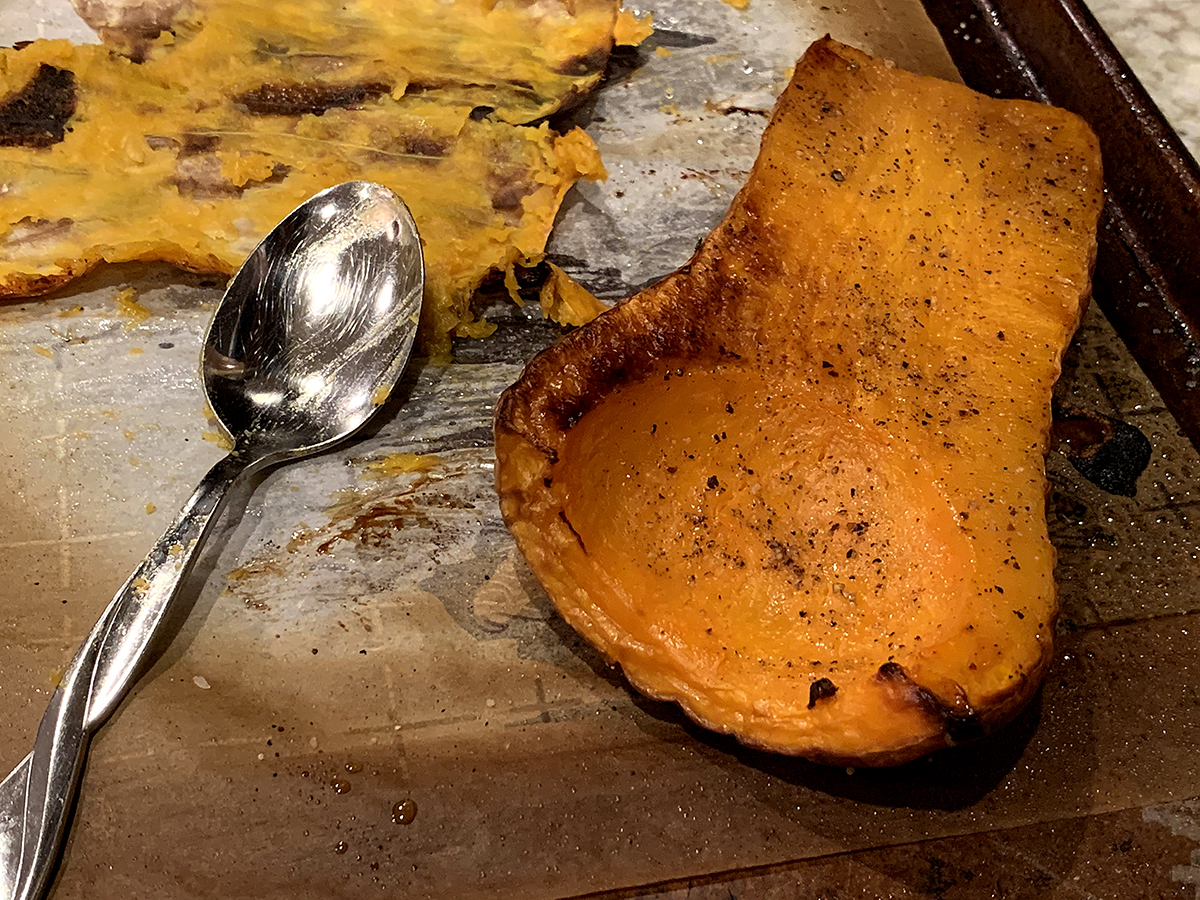 Roasted butternut squash halves with the flesh being scooped out.