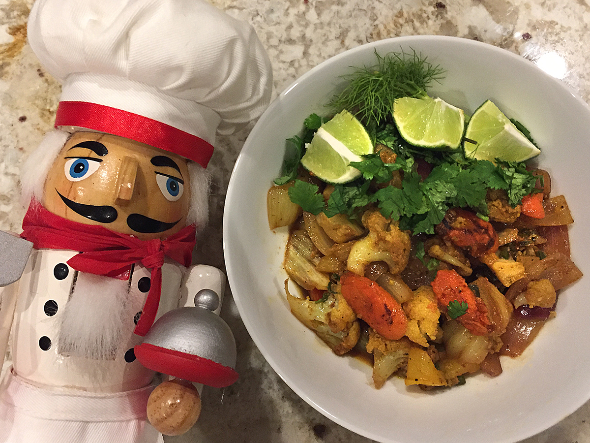 Cauliflower, fennel, carrots with lime wedges and fresh cilantro in a round white bowl. There's a nutcracker who looks like a chef in the foreground.