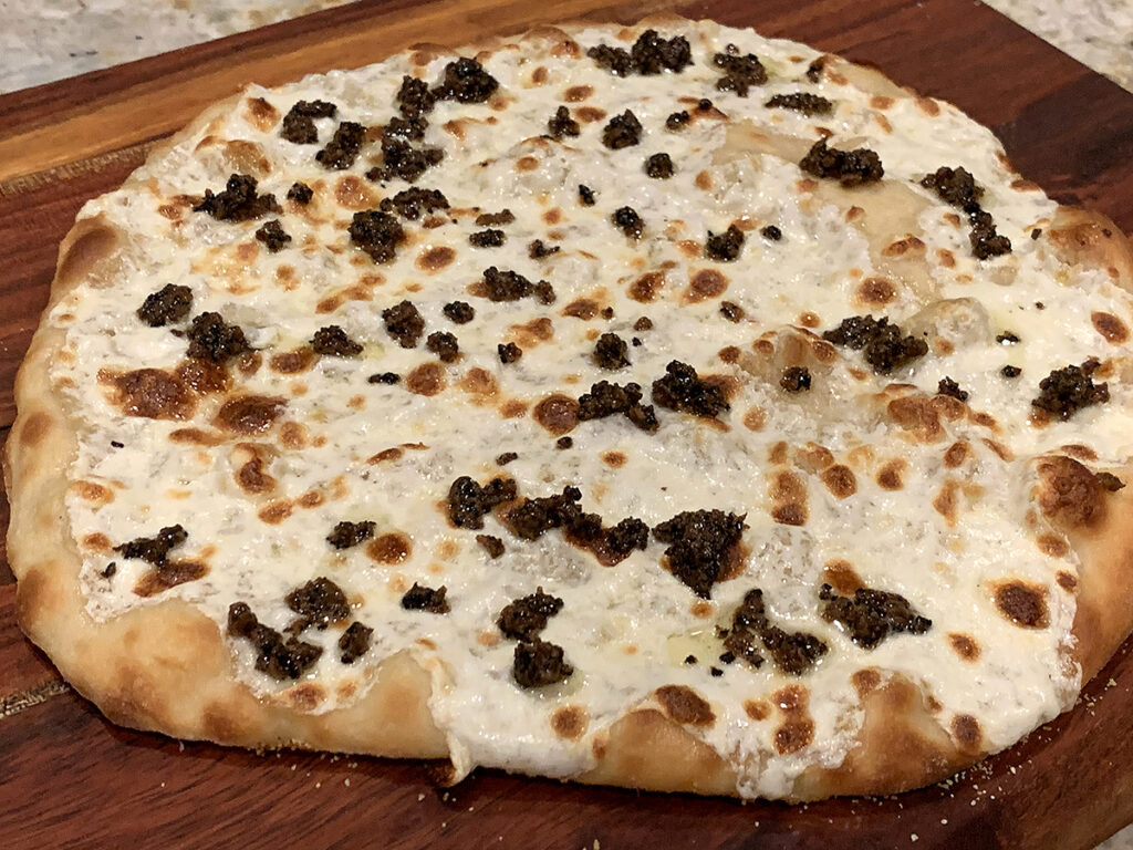cooked pizza dough with melted cheese and dollops of minced truffle on a wood cutting board.