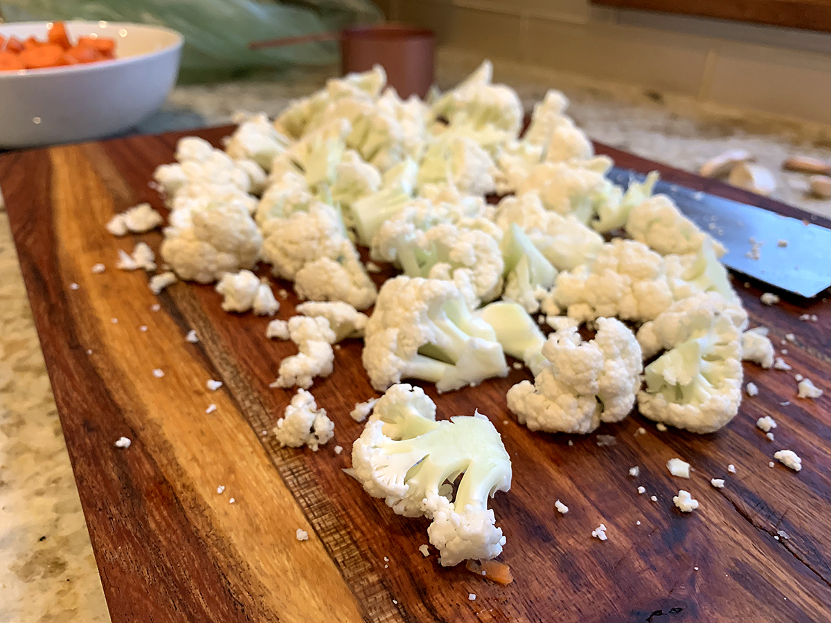 Cauliflower cut into large, bite size pieces on a wood cutting board.