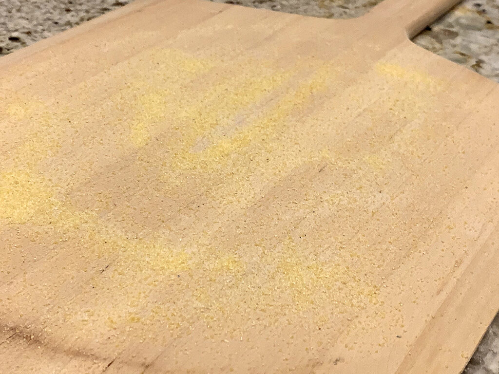 Generously dusted wood pizza peel with cornmeal