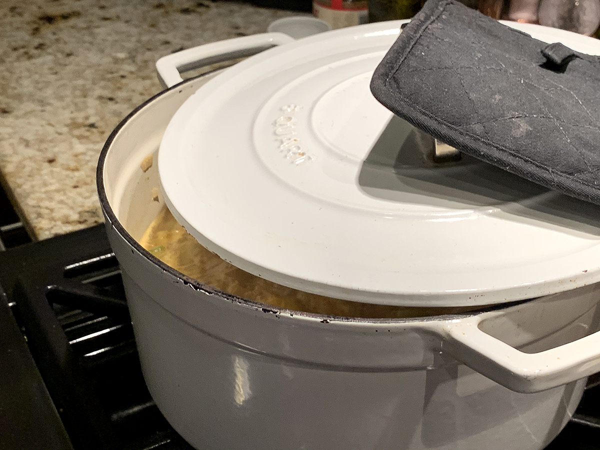 White dutch oven with lid partially closed and a square black pot holder on the handle.
