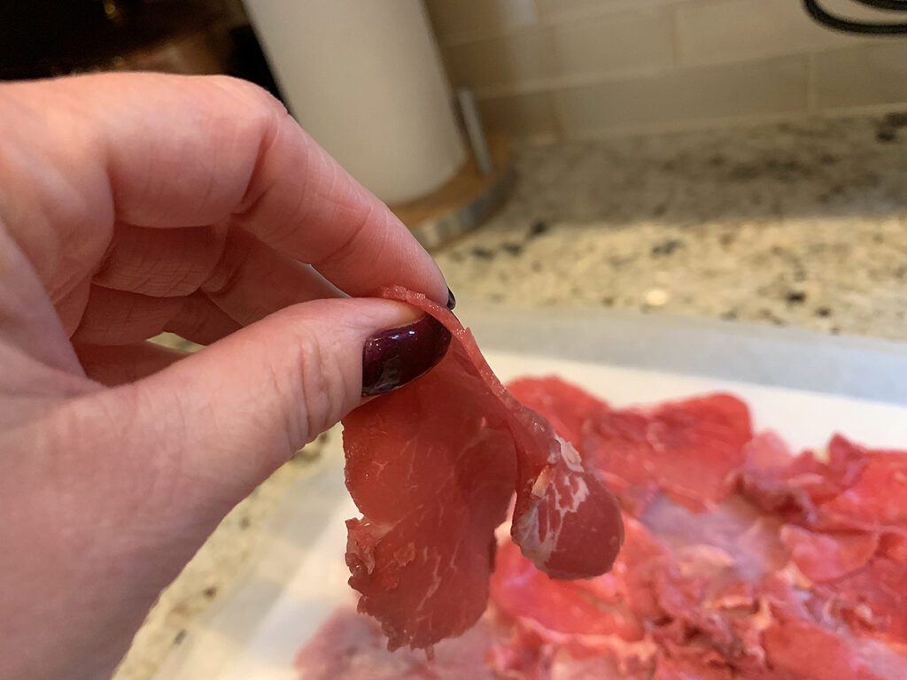 Female hand holding sliced raw beef to show how thick to slice it.
