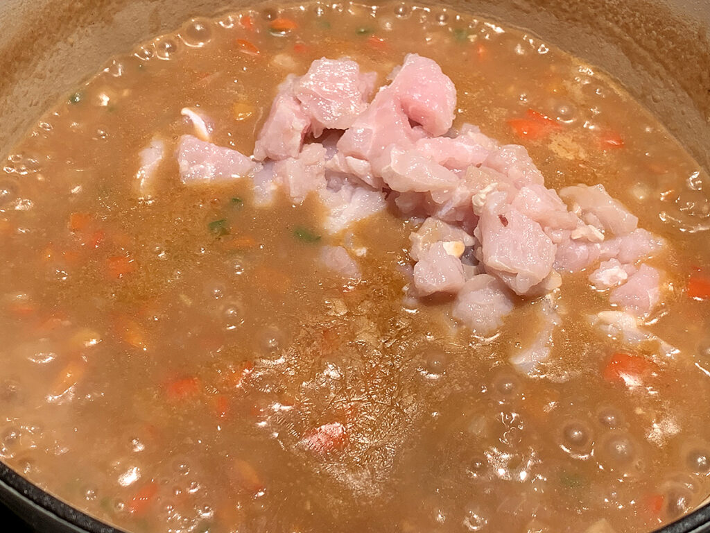 Raw pink alligator meat placed into etouffee sauce.