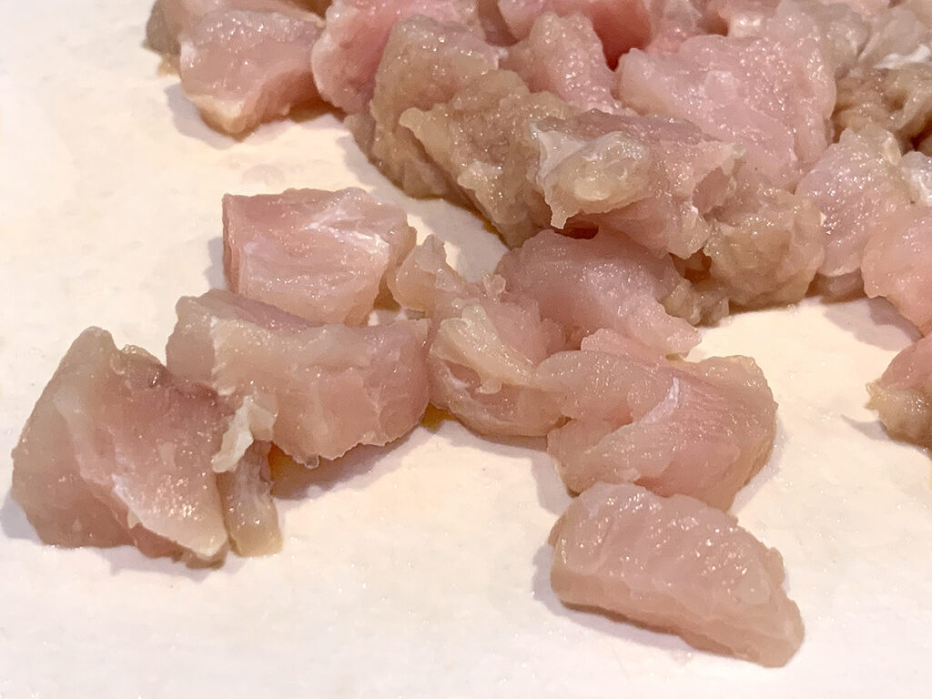 Pale pink alligator meat chunks on a white cutting board.