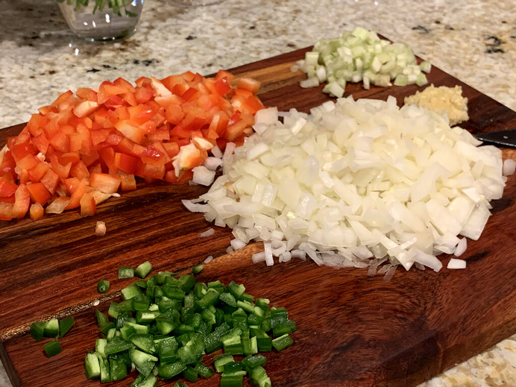 Piles of chopped red bell pepper, celery, yellow onion, green jalapeno and minced garlic.