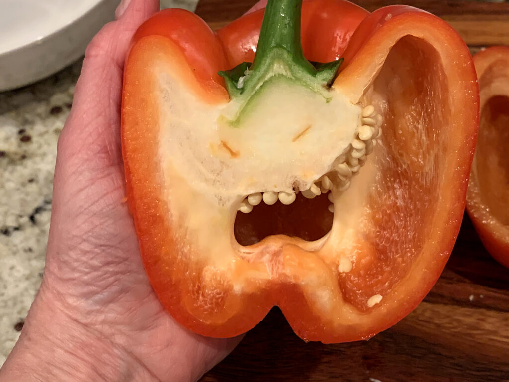 Red bell pepper sliced vertically in half. It looks like a face and the seeds are the teeth. 