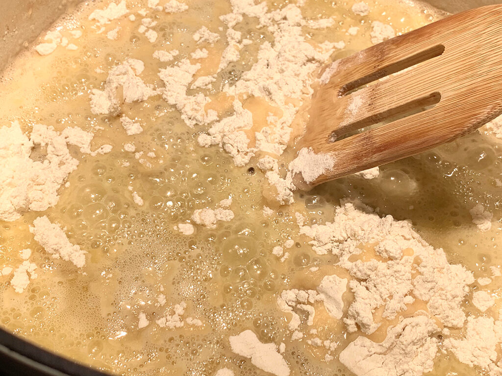 Flour and butter being mixed in a white dutch oven with a wooden spatula. 