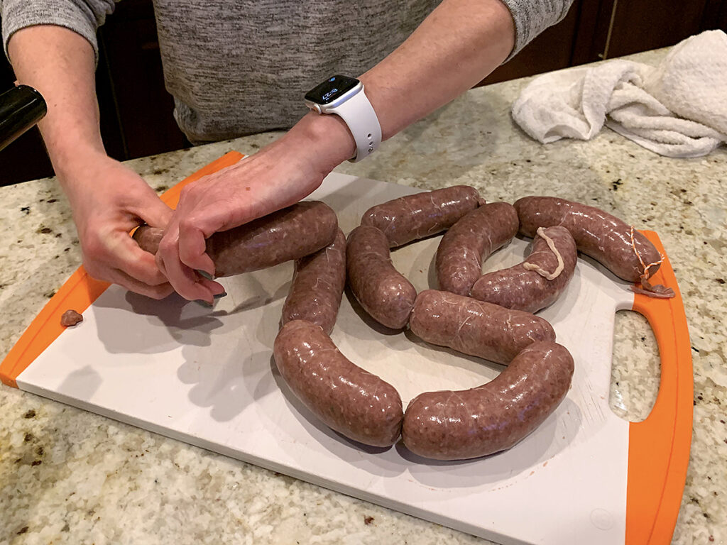 Hands twisting sausages into links.