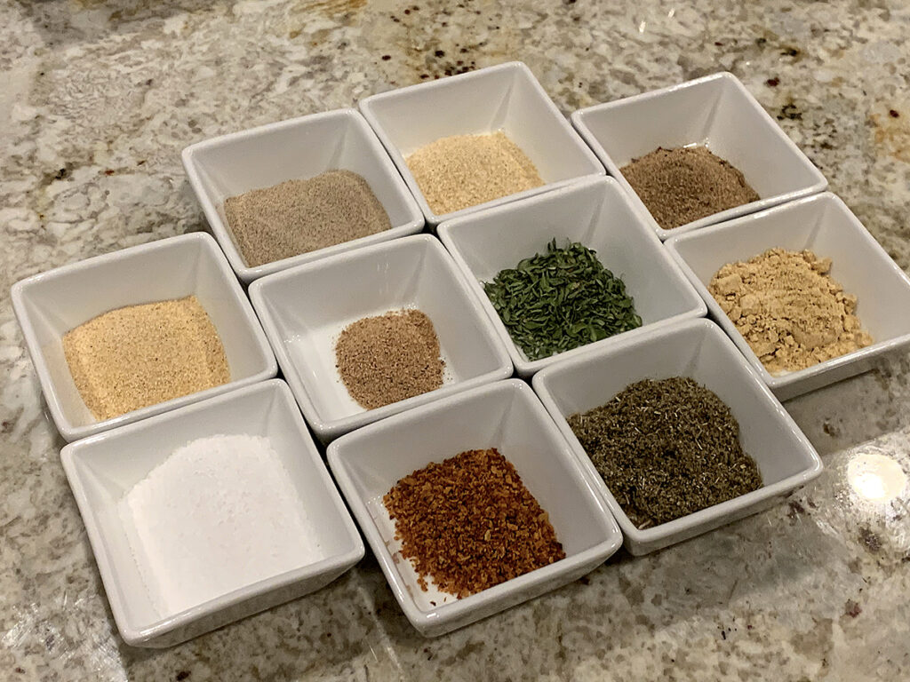 10 small square white ramekins with various spices and herbs in each.