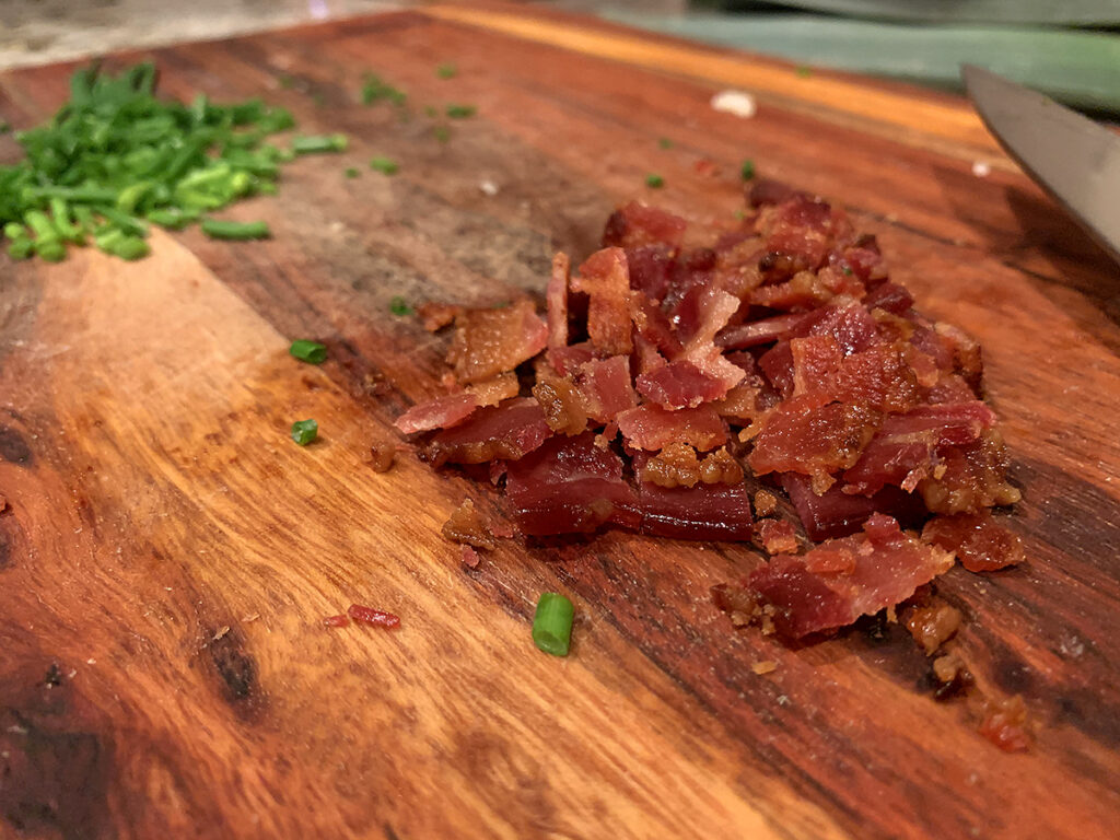Chopped bacon and chives on a wood cutting board.