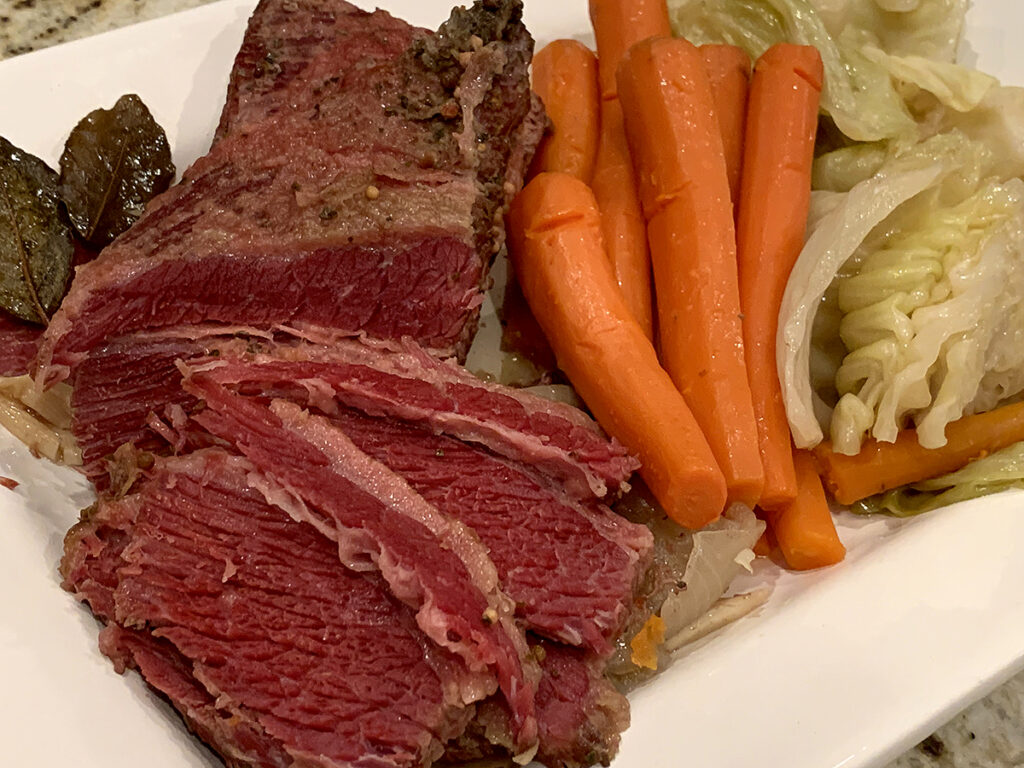 Large piece of corned beef partially sliced on a white platter with carrots and cabbage.